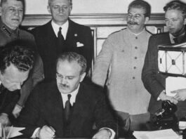 Foreign Minister Vyacheslav Molotov signs the pact. Behind him are Ribbentrop and Stalin